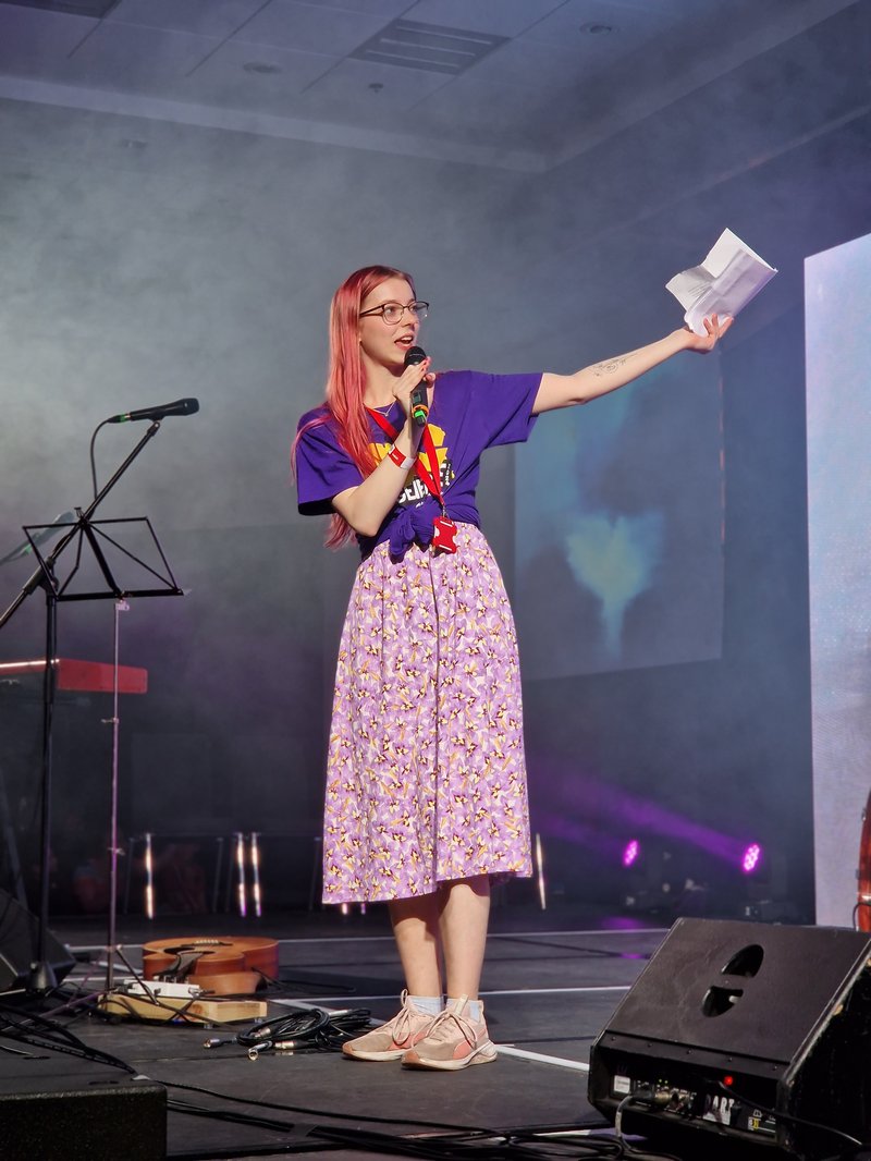 Bea Hulme, the Methodist Youth President, stands alone on a stage presenting to a crowd.