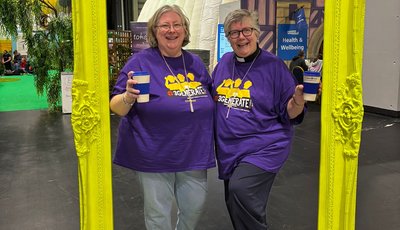 Two women, the President and Vice-President of the Methodist Conference, pose inside a yellow picture frame