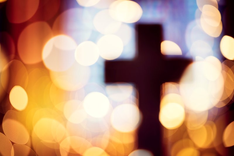 A blurred out cross with LED lights surround it, in front of a window.
