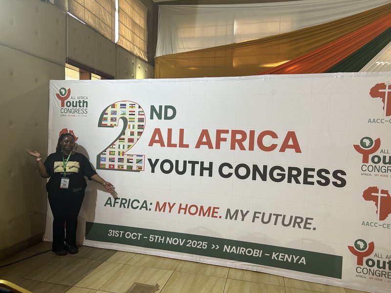 Woman standing to the left of a giant banner reading 2nd All African Youth Congress
