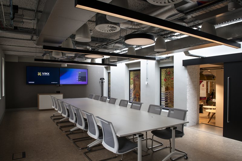 Large boardroom with a long table, grey chairs, dual presentation screens and an exposed industrial ceiling.