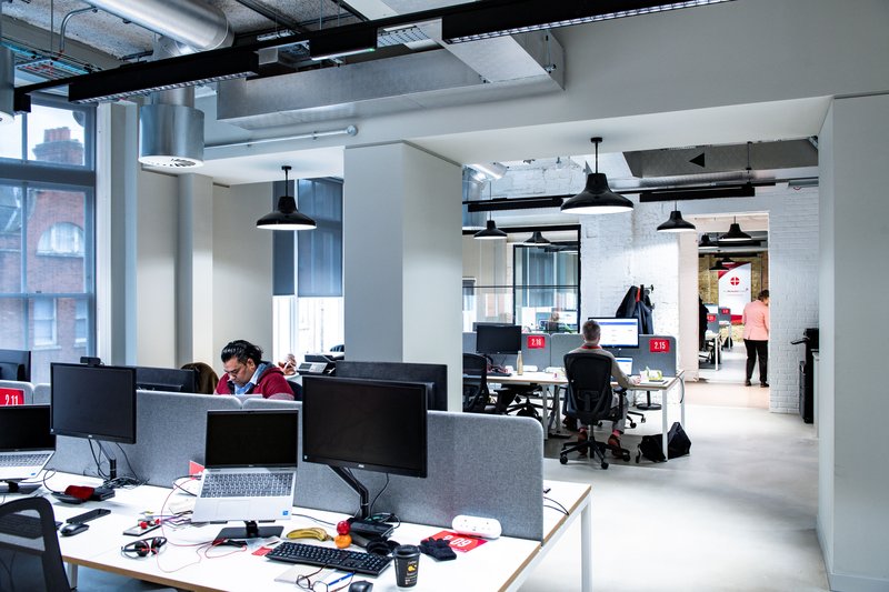 Open‑plan office at Methodist Church House with rows of computers and staff working under exposed ceiling ducts.