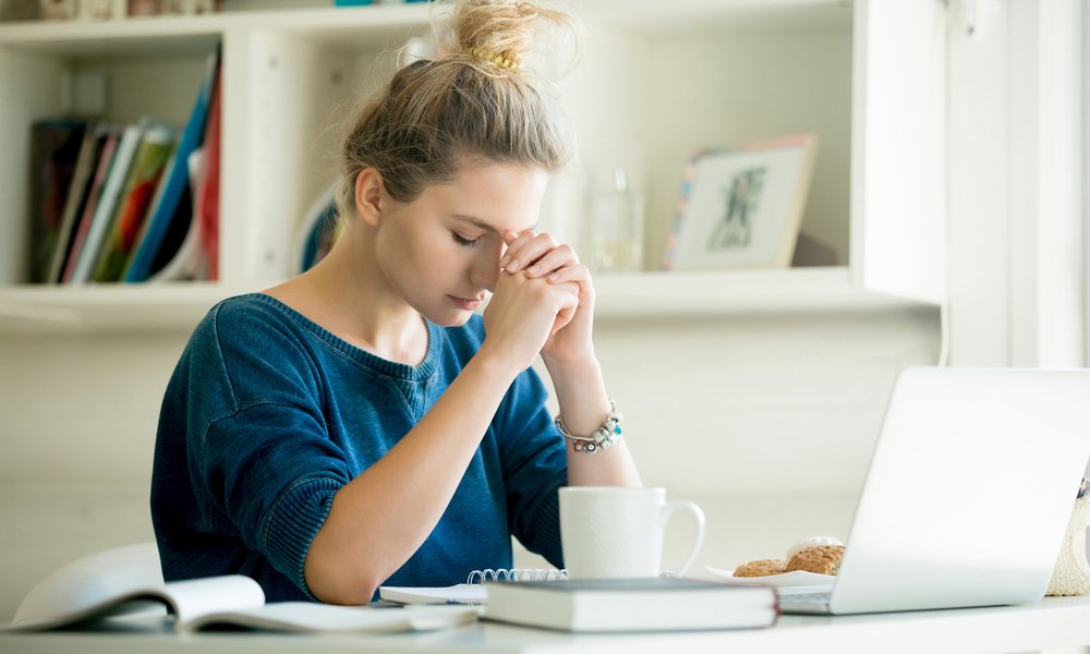 Young woman praying at desk with laptop
