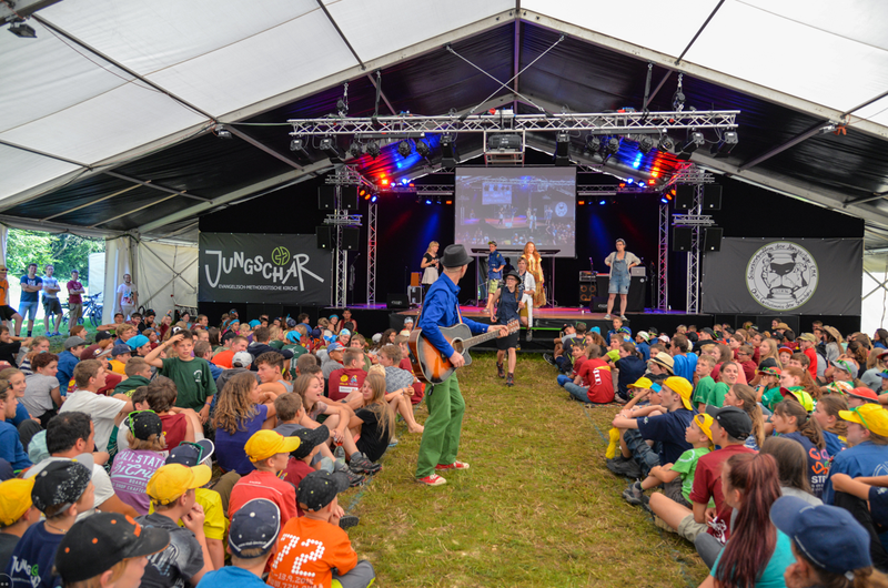 outdoor large tent full of young people facing a stage