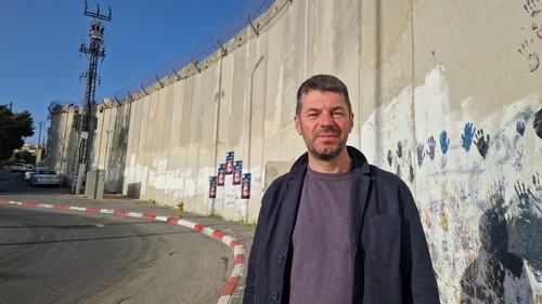 Mark Slaney stands in front of a security wall in Jerusalem