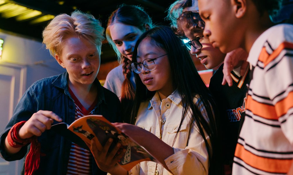 A group of teenagers gather around a magazine to read it.