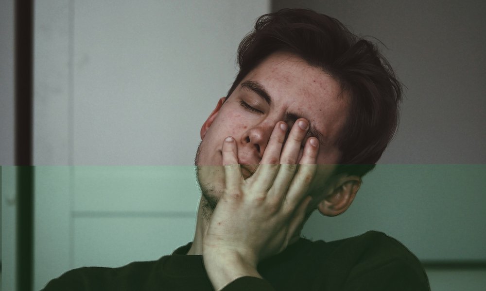 White man about 30 resting his face on his hand, looking tired.