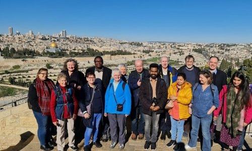 group of 12 people in a row standing on a hill above Jerusalem