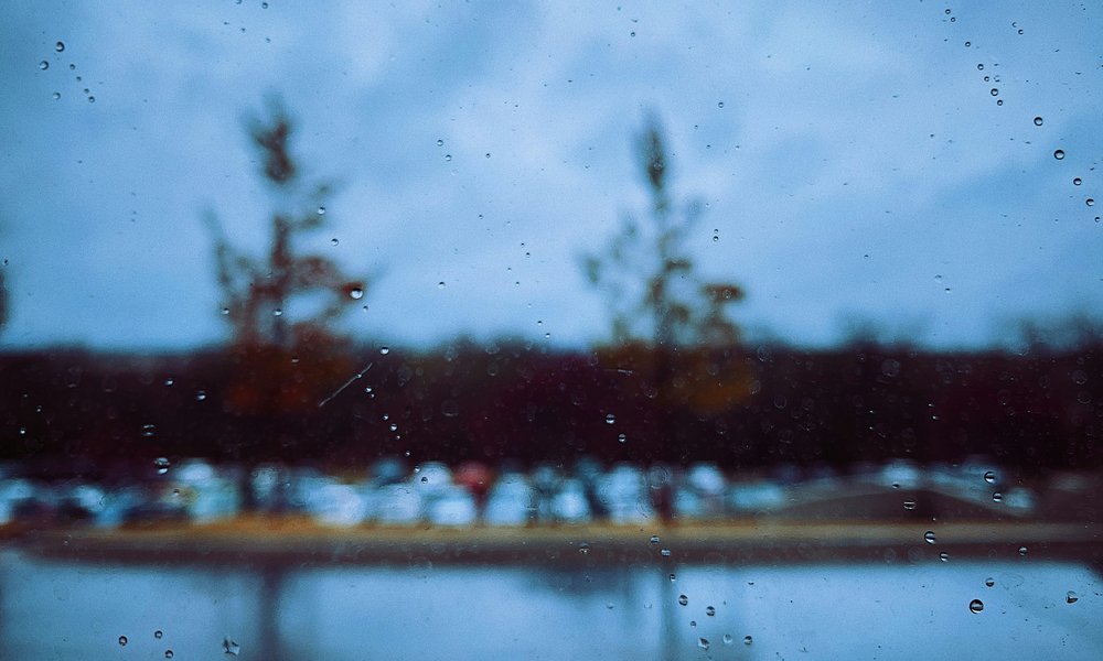 Photo: A window pane with rain trickling on the outside and a blurred outdoors behind