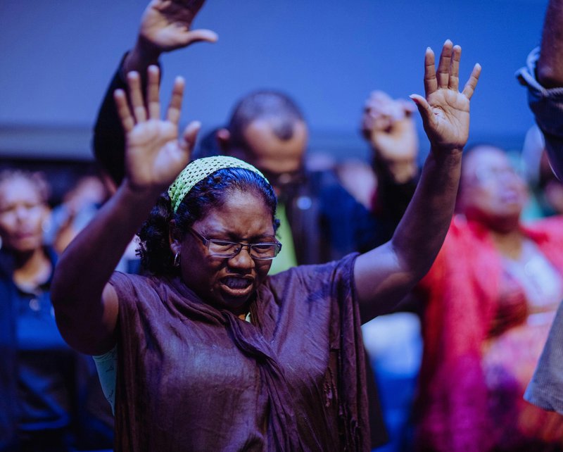 A black woman with her arms in the air during worship
