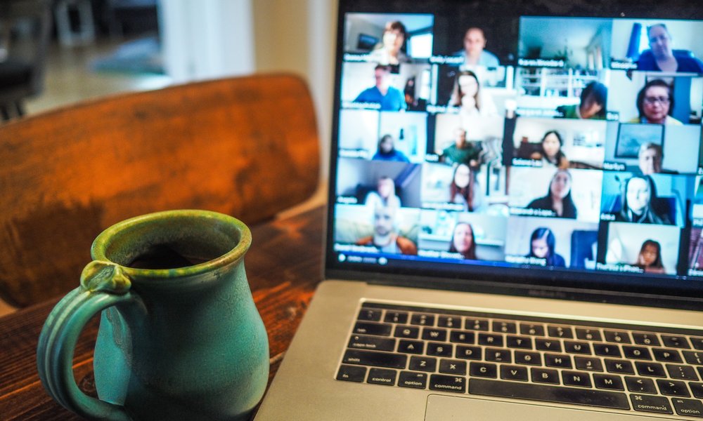 A mug stands next to a laptop showing a Zoom webinar taking place.