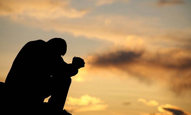 Silhoutte of a man crouched praying, with orange sunset behind him