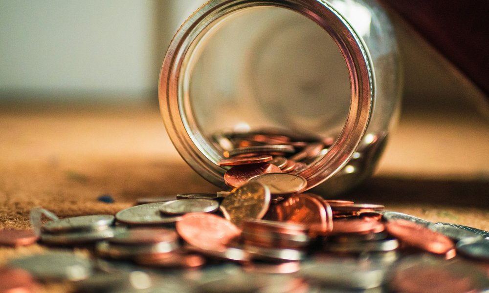 A jar tipped on its side, spilling coins out on to a wooden table