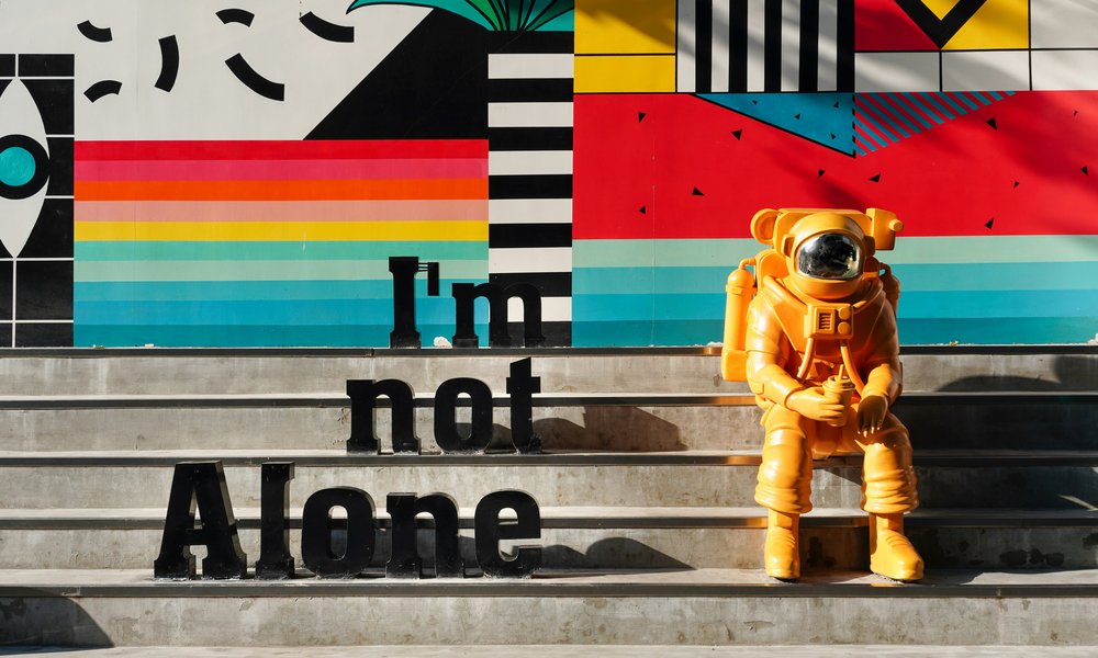 A person in an astronaut suit sits alone on a flight of steps. But letters on the steps say 'I'm not alone'.