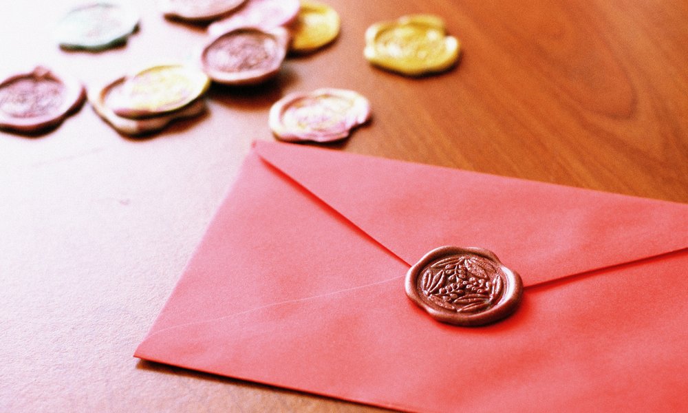 A red envelope with a wax seal on a wooden desk, with other wax seals piled up behind it.