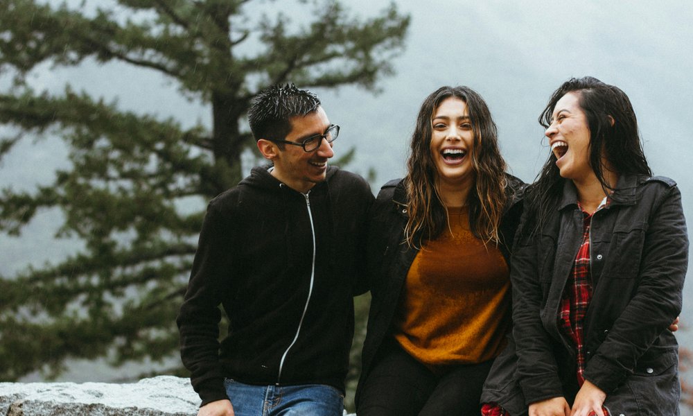 A photo of a man and two women sitting on a wall and laughing