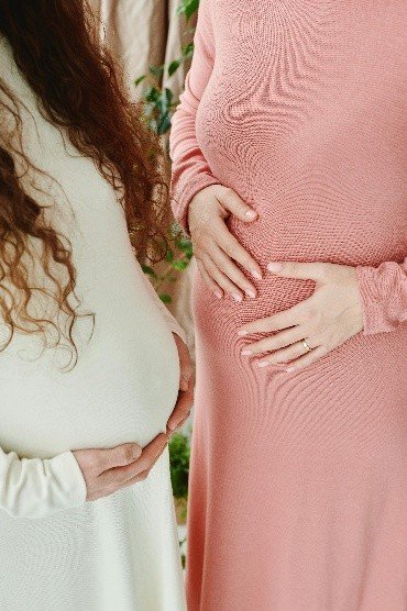 The pregnant bellies of two women, one dressed in pink the other in white.