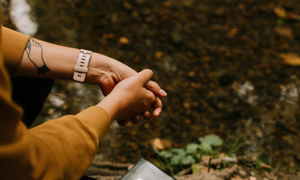 A view looking down on someone's hands held together as they prayer, outside the in forest.