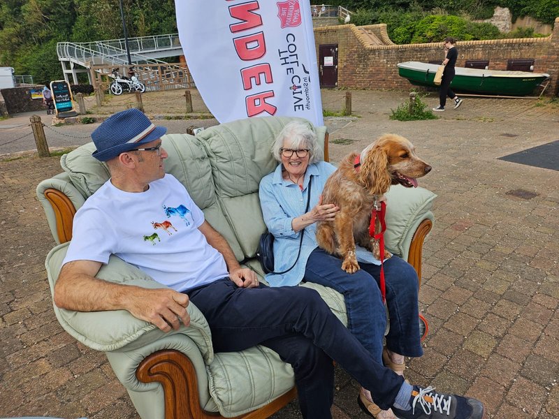 A sofa outside with a man and a woman sitting with a dog and chatting