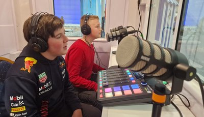 Two boys in their early teens talking into microphones in a recording booth