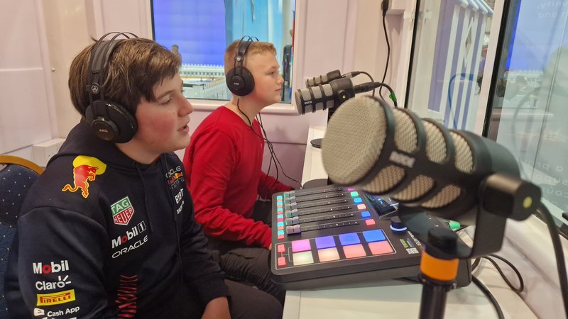 Two boys in their early teens talking into microphones in a recording booth