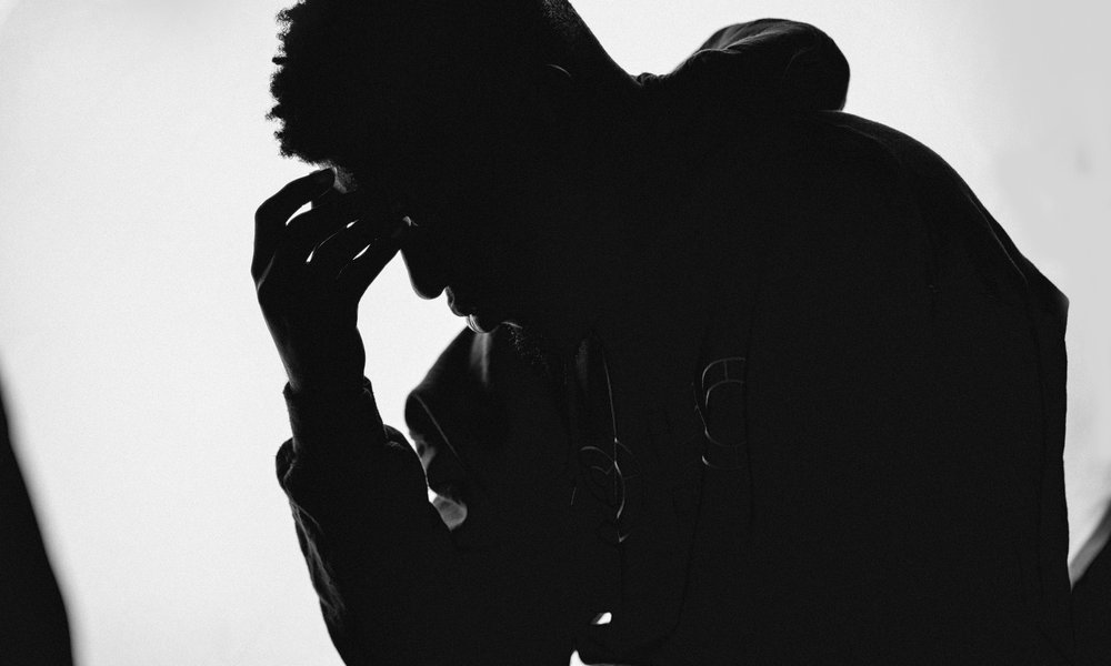 Black man in silhouette, with his head in his hand